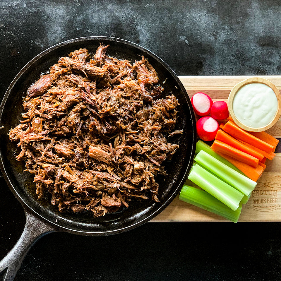 A pan of shredded buffalo beef beside cut carrots, celery, radishes and dip.